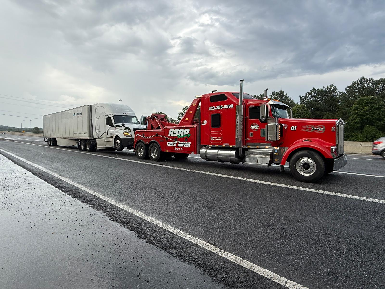 Red ASAP wrecker towing a semi on the highway